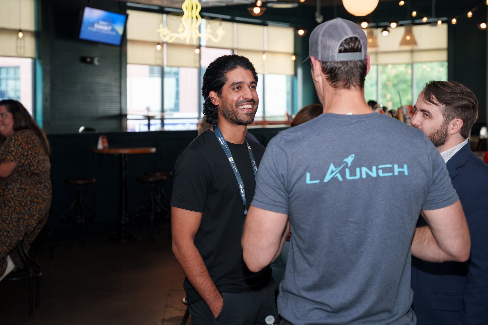 Attendees chatting at the Punch Bowl Social networking reception, with one person wearing a Launch t-shirt visible in the foreground